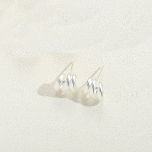 Detailed view of silver-plated multilayer coiled hoop earrings on a beige textured surface