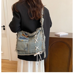 Detailed close-up of blue washed denim crossbody bag featuring frayed edges and lace-up design