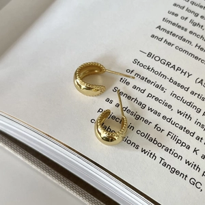 Elegant gold C-shaped hoop earrings with milgrain edges on a vintage book