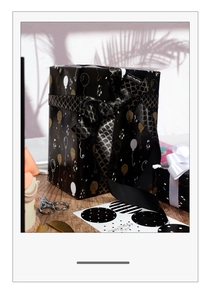 Detail of black gift wrap with gold balloons, scales ribbon, and birthday stickers