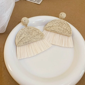 Gros plan de boucles d'oreilles à pompons en raphia tissées à la main, style bohème.