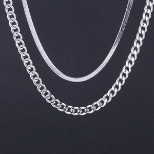 Close-up of dual-layer silver steel jewelry featuring flat snake chain and bold curb chain
