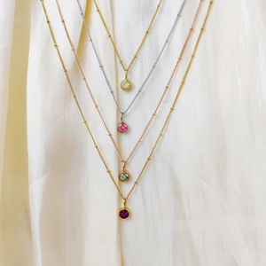 Detail of layered stainless steel necklaces featuring colorful round birthstone pendants.