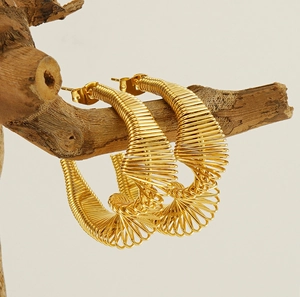 Detailed view of gold spiral spring hoop earrings with textured wire wrap on wood
