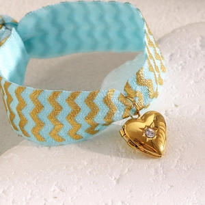 Macro shot of light blue patterned ribbon with gold heart locket and sparkling zircon