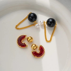 Elegant gold earrings with black round spheres, pearl tassels, and red resin studs