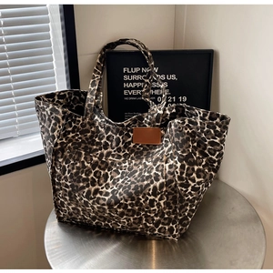 Close-up of leopard print canvas tote bag with brown leather patch and metal rivet detail