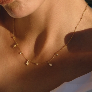 Gold lightning bolt and zircon necklace worn by a model in soft natural sunlight