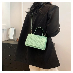 Detail of mint green square bag featuring repetitive M patterns and golden hardware