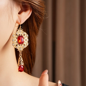 Close-up of vintage gold hollow-out drop earrings with red rubies and crystal accents