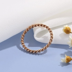 Detailed view of a rose gold twisted rope ring on a blue background with dry flowers