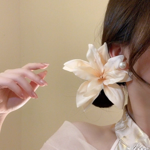 Detail view of large white fabric lily hair clip with pearl accent on model hair