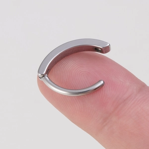 Macro shot of silver stainless steel navel ring on fingertip with smooth metallic finish