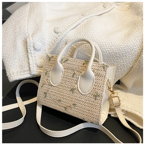 Detail of floral embroidery on a straw bag with white faux leather handle and metal hardware