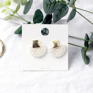Close-up of golden square brushed earrings with white pearl clusters on a card