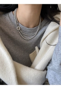 Detail of a double-layer silver beaded necklace with a square shell pendant on a model