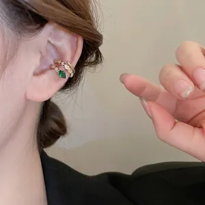 Gold plated snake-like ear bone clip with green zircon droplet worn on model's ear