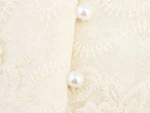 Gros plan sur la dentelle beige et les boutons de perles élégants sur la robe