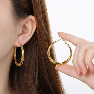 Close-up of model wearing large 18K gold plated twisted C-shape hoop earrings in metal