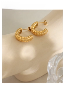 Macro shot of gold C-shape hoop earrings with vintage textured ribbed surface