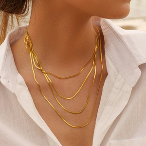 Close-up of four-layered 5mm golden flat snake bone chains worn by a model