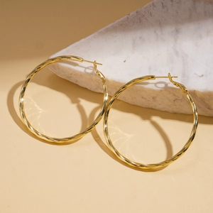 Macro detail of 14k gold plated twisted hoop earring on white marble stone display