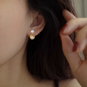 Close-up of elegant crossover pearl stud earring with golden twisted metal design