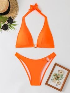 Flat lay of bright orange halter bikini set with ring details and beach accessories