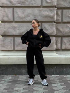 Women's black two-piece tracksuit with hooded zip jacket and joggers featuring golden crest