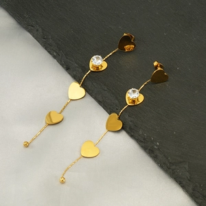 Detailed macro view of gold long tassel earrings with heart pendants and cubic zirconia