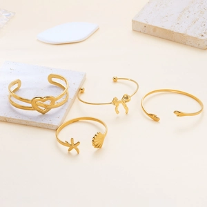 Set of four gold stainless steel open bangles with heart, bow, and ocean theme designs