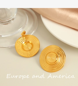 Close-up of golden round earrings with concentric texture on silk and glass background