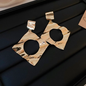 Detail of gold geometric square earrings with hammered texture on black leather background