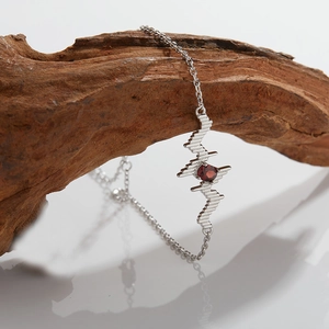 Detail showing silver heartbeat necklace with red gemstone on artistic wooden branch