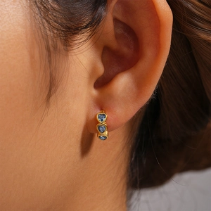 Detailed view of small gold hoop earrings featuring three sparkling blue heart crystals