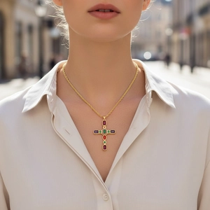 Dettaglio del ciondolo a croce dorata con zirconi colorati indossato su camicia bianca