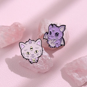 Detailed close-up of cute purple enamel cat and bat pins on pink gemstone base