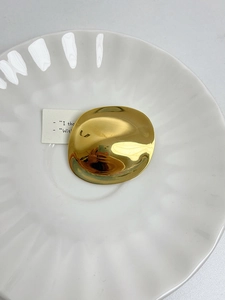Detailed view of a golden irregular round brooch displayed on a white ceramic plate