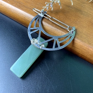 Detail of silver crescent moon hair clip with a green rectangular natural crystal pendant