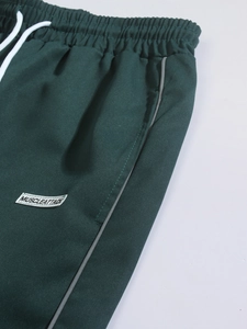 Detail of dark green woven trousers with elastic drawstring waist and pocket label
