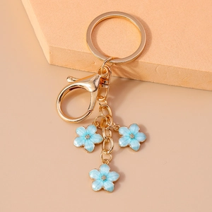 Detailed macro view of golden keychain featuring three blue enamel flowers with gold stamens