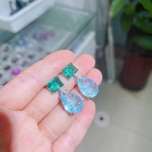 Macro detail of bicolored gemstone earrings featuring emerald rectangle and blue teardrop