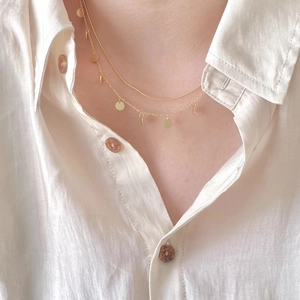 Double-layer gold snake chain necklace with circular sequins on a white linen shirt