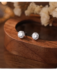 Macro shot of S999 silver sparkling zircon stud earrings on a minimalist wooden base