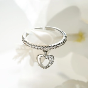 Macro shot of silver open ring with pave-set crystals and a dangling hollow heart charm