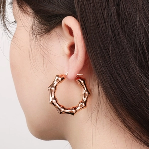 Detail of rose gold U-shaped bamboo textured hoop earrings on a female model