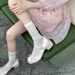 Pink satin Mary Jane block heels with bow detail shown on a green velvet bench