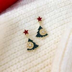 Detailansicht der Weihnachtsbaum-Ohrringe mit Goldflocken auf beigem Strickpullover