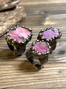 Three vintage bronze rings with irregular raw purple stones on dark wood table