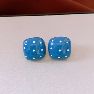 Detailed view of blue and white polka dot square stud earrings on beige leather texture
